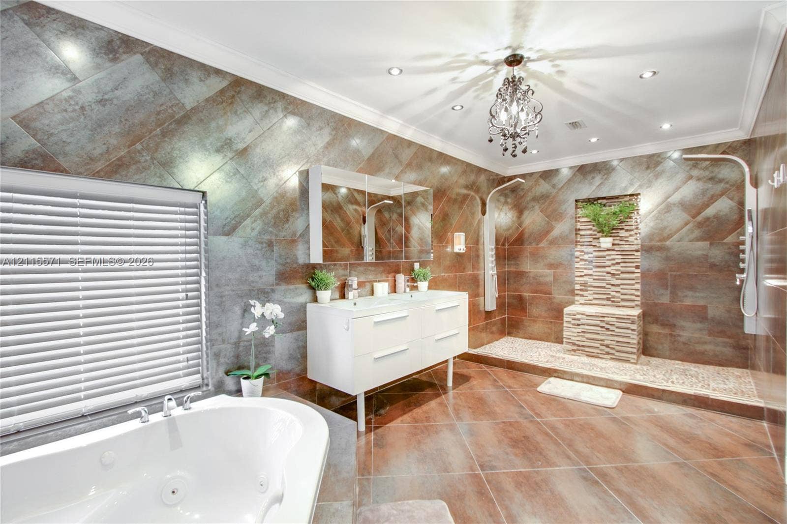 2001 NE 122nd Road, North Miami, FL 33181 Bathroom featuring large-format diagonal tile wall cladding, a double-basin floating vanity, a jetted soaking tub, a multi-head walk-in shower with pebble-stone flooring, and a crystal chandelier