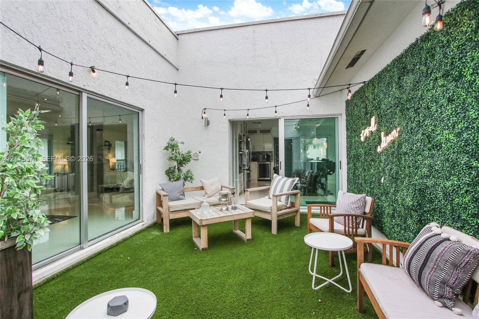 2001 NE 122nd Road, North Miami, FL 33181 Private courtyard featuring high stucco walls, artificial turf, sliding glass doors, and a decorative greenery wall