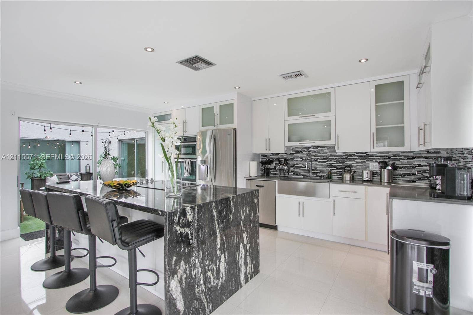 2001 NE 122nd Road, North Miami, FL 33181 Kitchen featuring white cabinetry, stone-topped central island with waterfall edge, stainless steel farmhouse sink, tiled backsplash, and recessed lighting