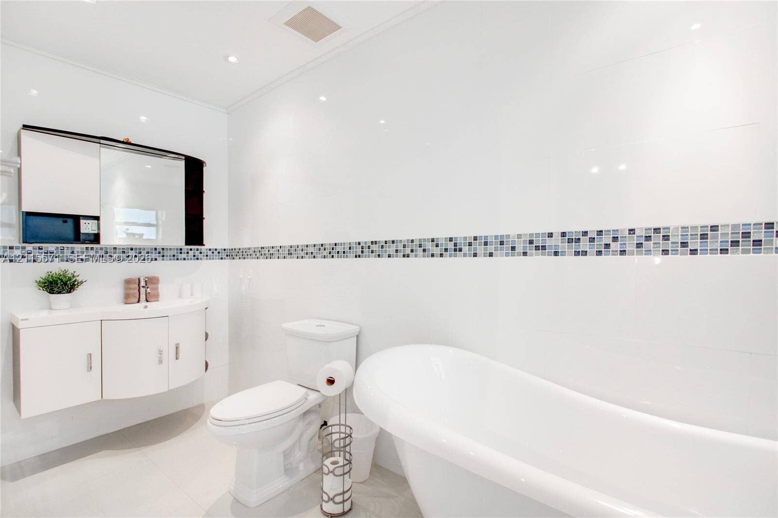 2001 NE 122nd Road, North Miami, FL 33181 Freestanding soaking tub, wall-mounted curved vanity with integrated storage, built-in medicine cabinet, and decorative mosaic tile backsplash