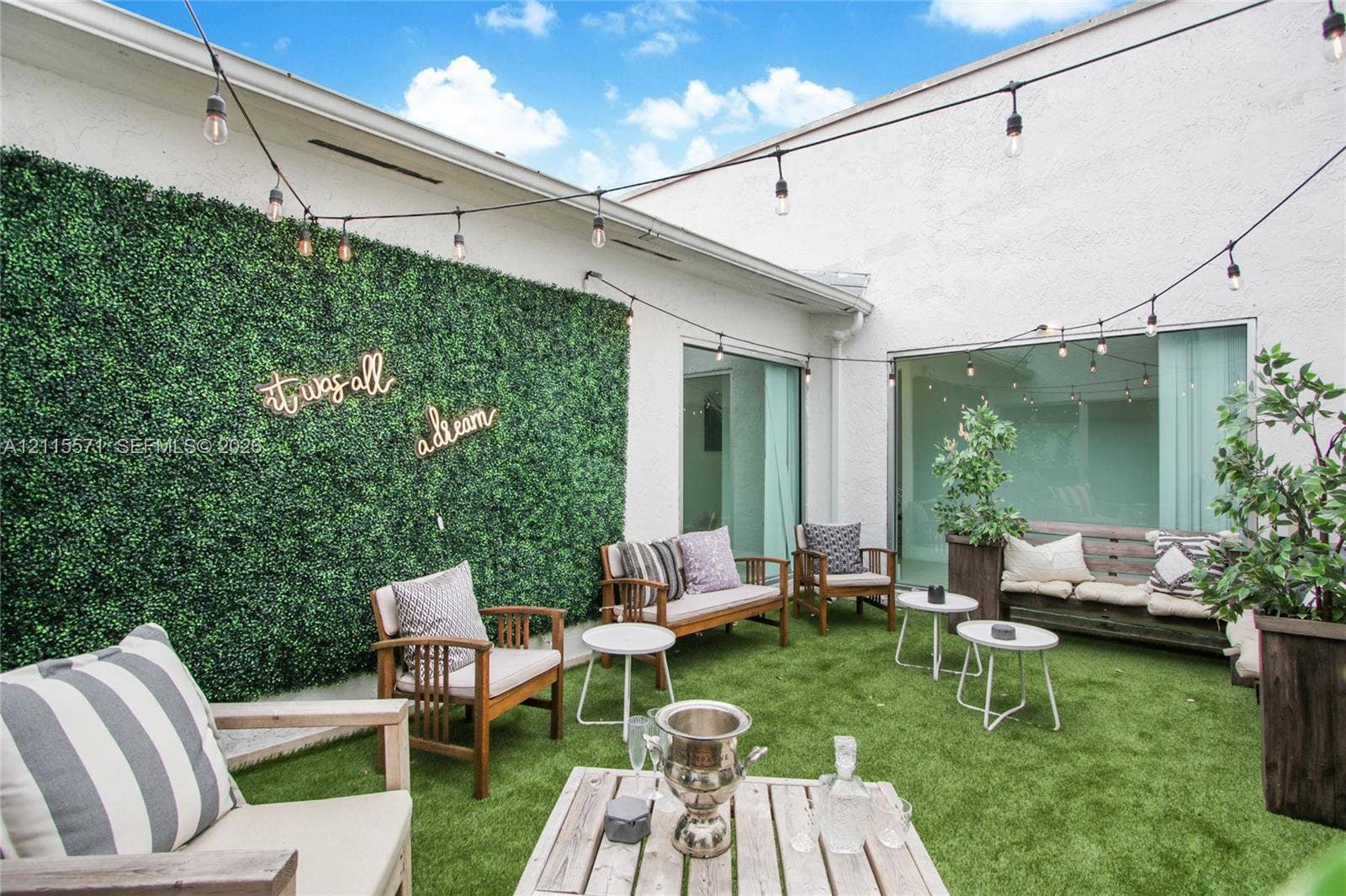 2001 NE 122nd Road, North Miami, FL 33181 Private courtyard featuring synthetic turf, decorative greenery wall, and overhead string lighting