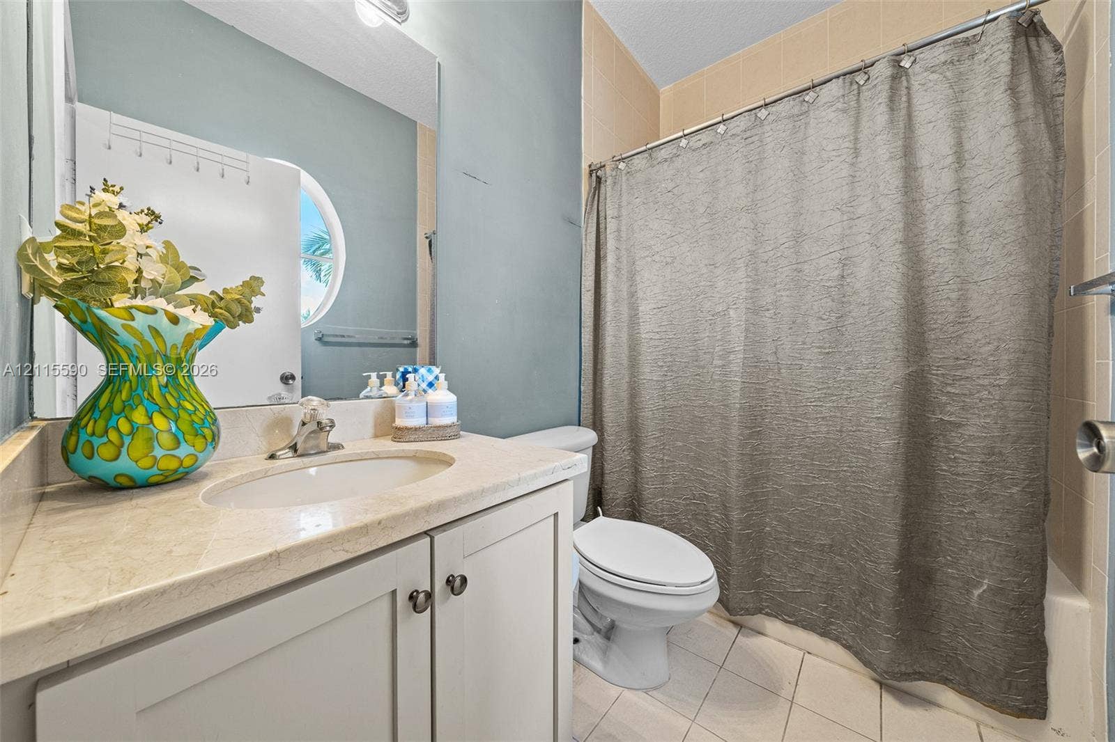 4948 Tradewinds Terrace, #504, Dania Beach, FL 33312 Bathroom featuring a vanity with a stone countertop, an integrated oval sink, a large wall-mounted mirror, a circular window, and tiled flooring