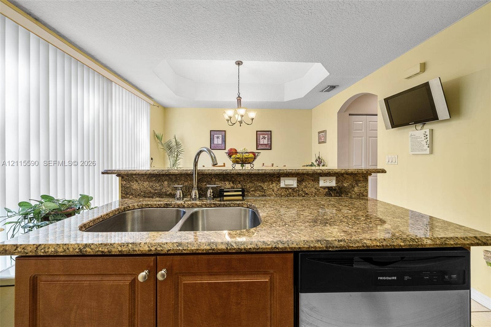 4948 Tradewinds Terrace, #504, Dania Beach, FL 33312 Kitchen featuring stone-finish countertops, stainless steel dual-basin undermount sink, gooseneck faucet, stained wood cabinetry, and recessed tray ceiling with a multi-light chandelier