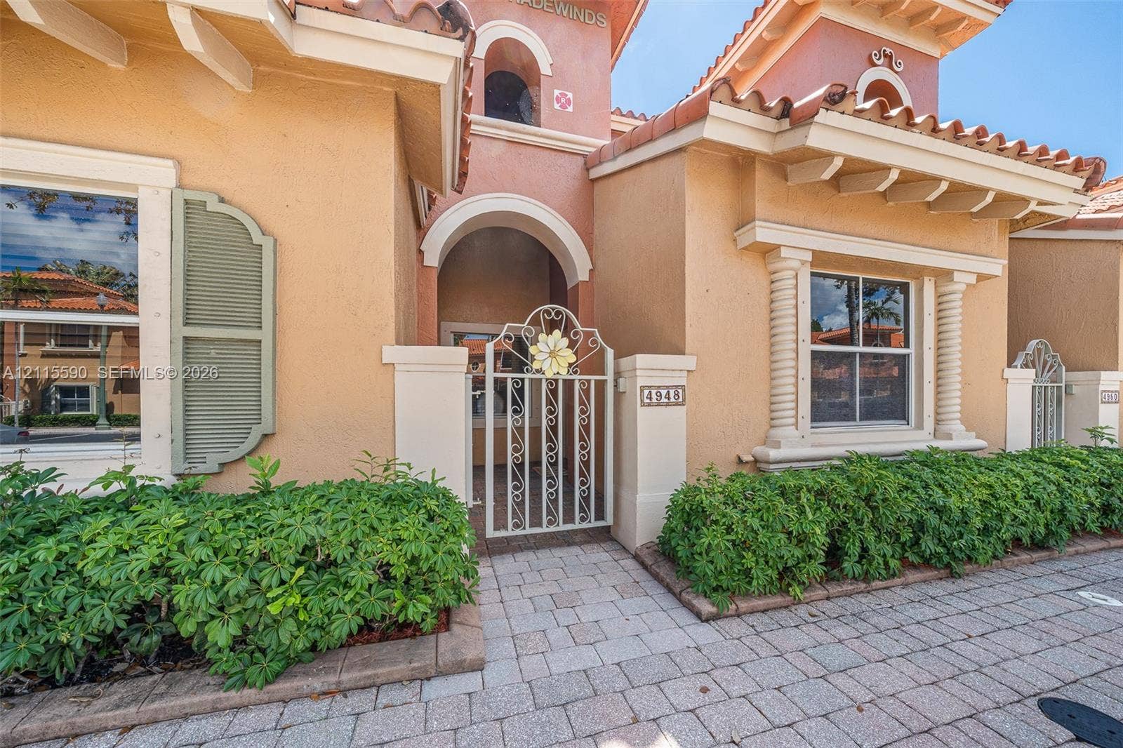 4948 Tradewinds Terrace, #504, Dania Beach, FL 33312 Stucco exterior featuring arched architectural detailing, decorative metal gate, pilasters, mission-style roof tiles, and paver walkway