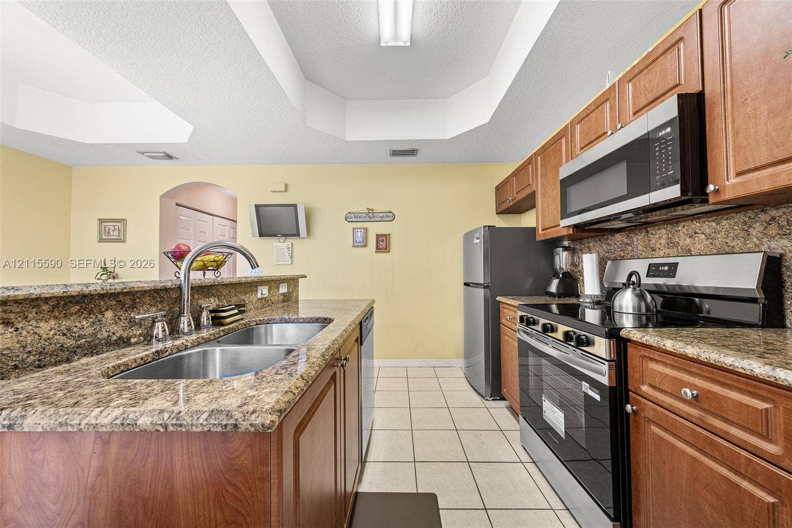 4948 Tradewinds Terrace, #504, Dania Beach, FL 33312 Kitchen featuring stained wood cabinetry, stone-finish countertops, stainless steel appliances, dual-basin stainless steel sink, and ceramic tile flooring