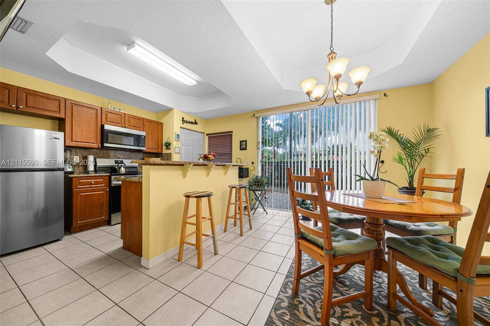 4948 Tradewinds Terrace, #504, Dania Beach, FL 33312 Kitchen featuring wooden cabinetry, stone-surface breakfast bar, stainless steel refrigerator, tile flooring, and a tray ceiling with a multi-arm chandelier