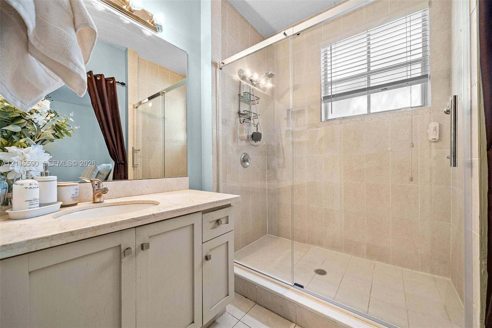 4948 Tradewinds Terrace, #504, Dania Beach, FL 33312 Bathroom featuring a vanity with an integrated sink and neutral countertop, walk-in shower with floor-to-ceiling tile, sliding glass shower door, and wall-mounted vanity mirror with integrated lighting