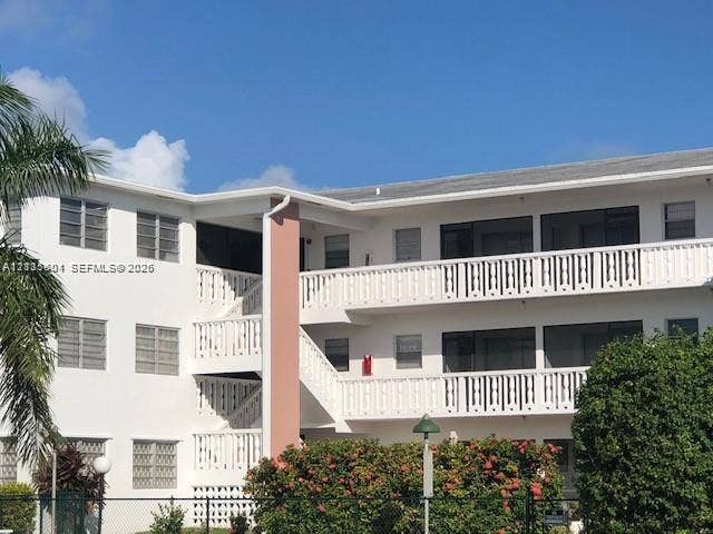 Multi-story exterior featuring white stucco siding, tiered balconies with white railings, screened enclosures, and louvered windows