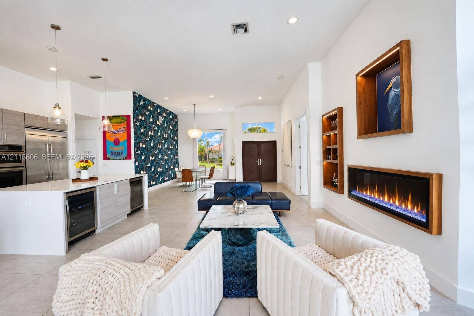 2652 Palmer Place, #2652, Weston, Weston, FL 33332 Open-concept interior featuring large-format tile flooring, a wall-mounted linear electric fireplace with wood trim, built-in recessed shelving, a center island with integrated wine refrigeration, and a patterned accent wall