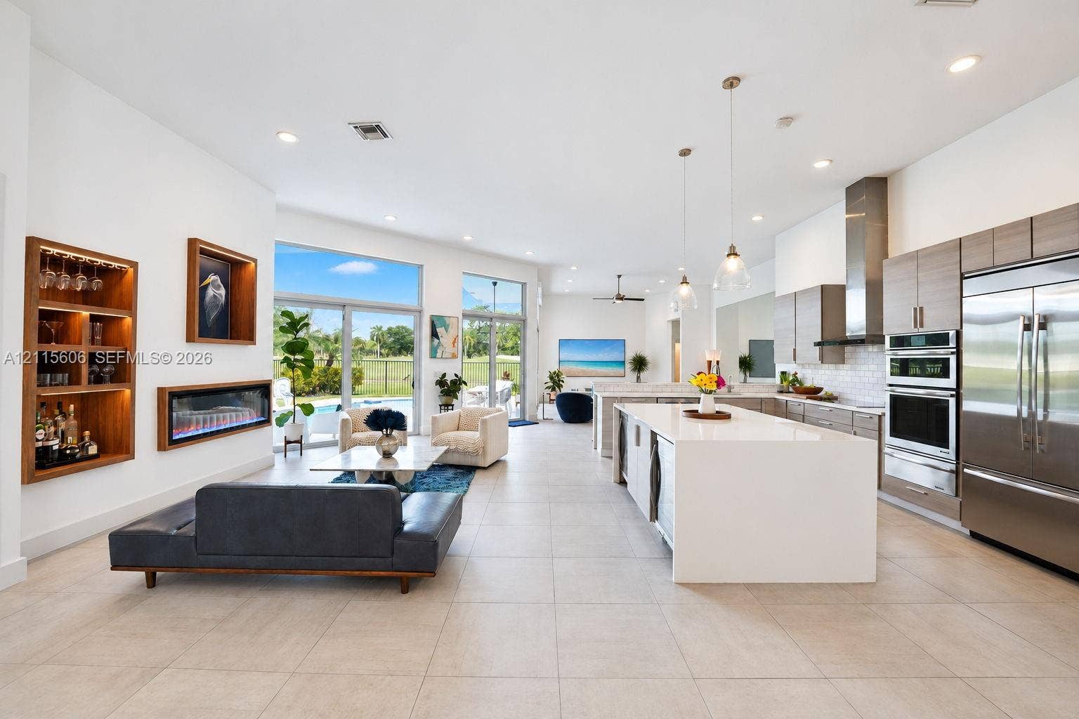 2652 Palmer Place, #2652, Weston, Weston, FL 33332 Open-concept living space featuring a central kitchen island with waterfall-edge stone countertop, built-in recessed shelving, integrated linear fireplace, and large glass sliding doors