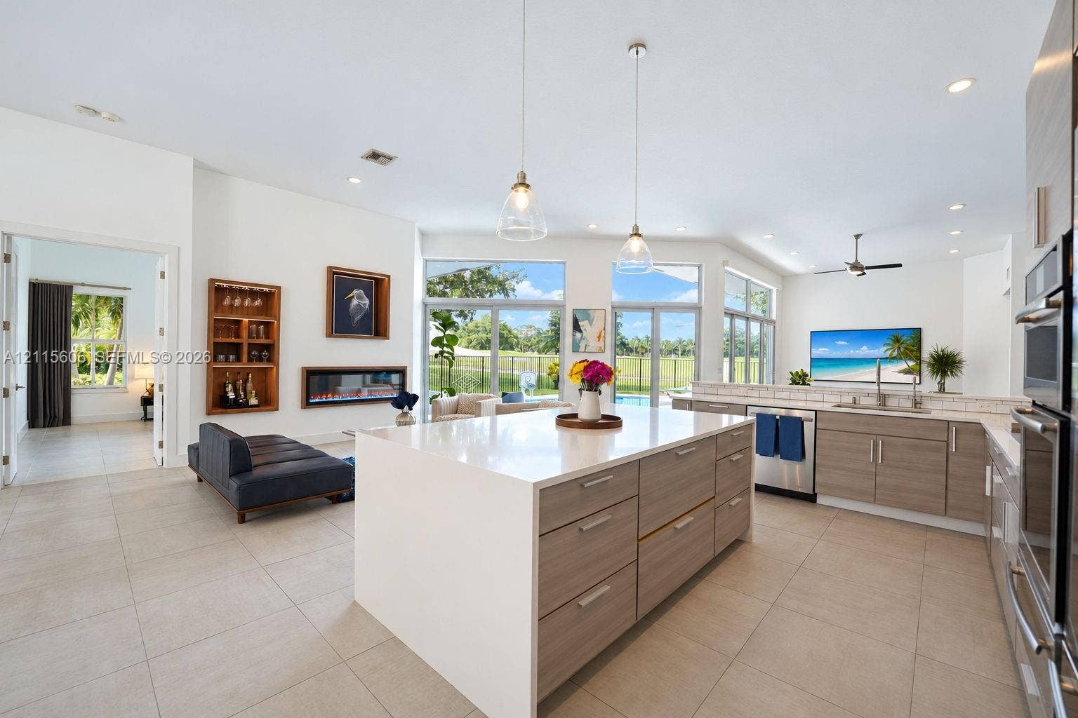 2652 Palmer Place, #2652, Weston, Weston, FL 33332 Open-concept kitchen featuring an oversized island with quartz countertops, wood-finish cabinetry, built-in stainless steel double ovens, recessed lighting, and a wall-mounted electric fireplace