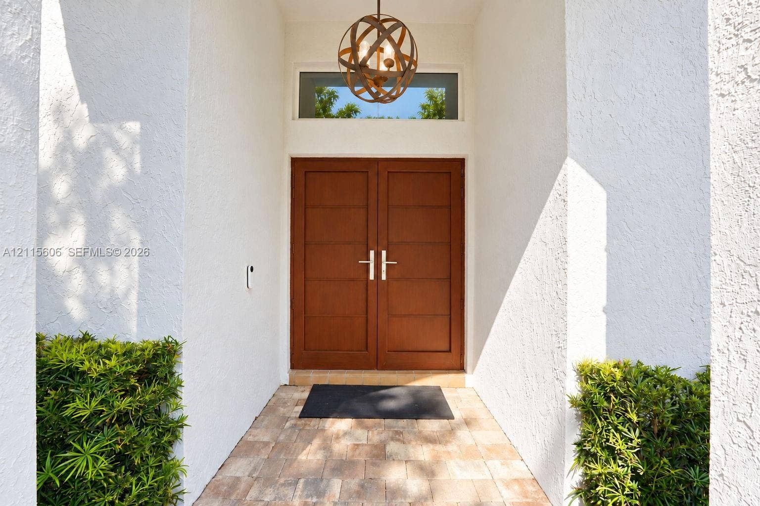 2652 Palmer Place, #2652, Weston, Weston, FL 33332 Entryway featuring double wood-finish doors with horizontal paneling, a circular metal orb pendant light fixture, a rectangular transom window, and stone paver flooring