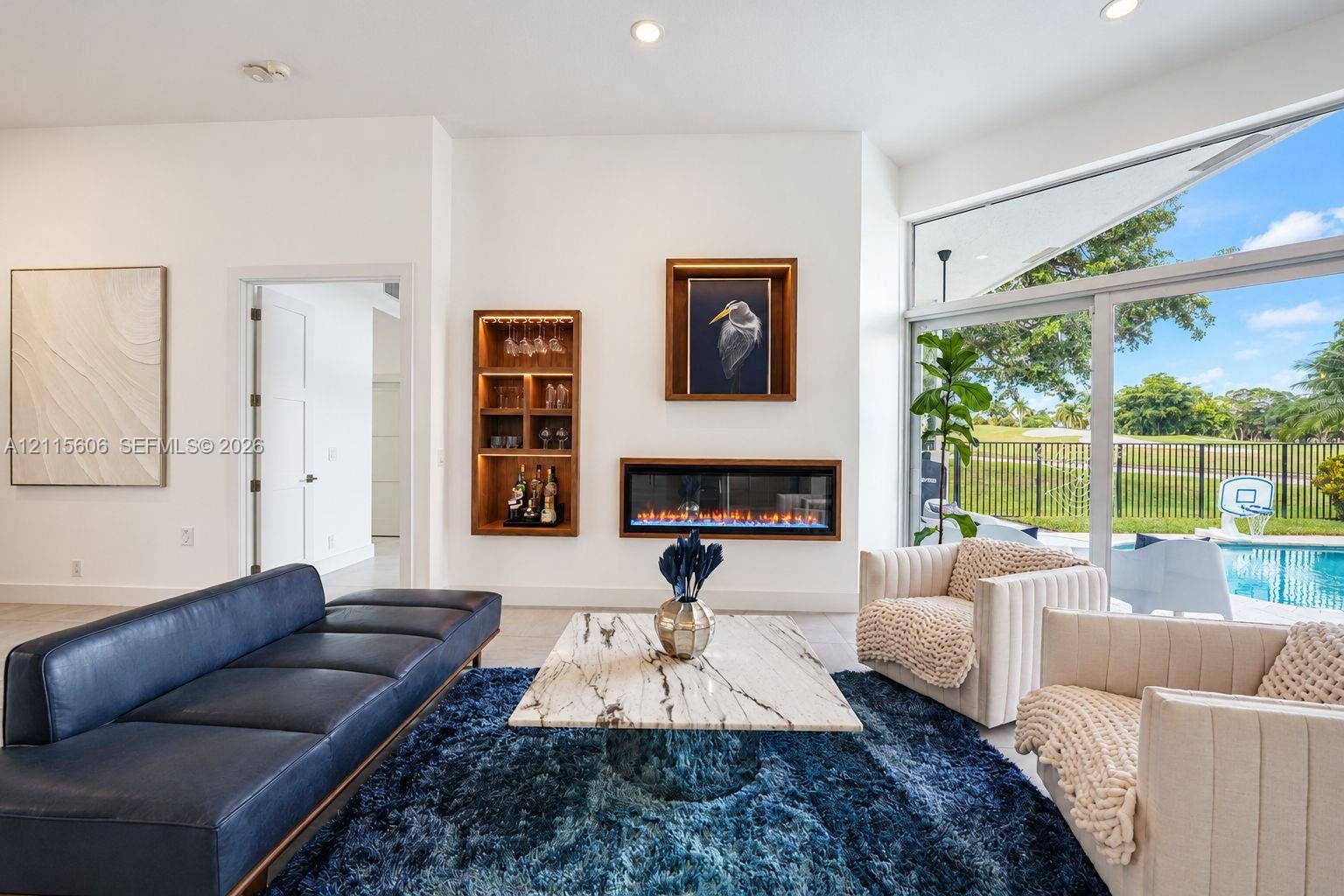 2652 Palmer Place, #2652, Weston, Weston, FL 33332 Modern living space featuring a built-in electric fireplace, recessed wood-trimmed shelving, large-format tile flooring, and floor-to-ceiling glass sliding doors with pool and golf course exposure