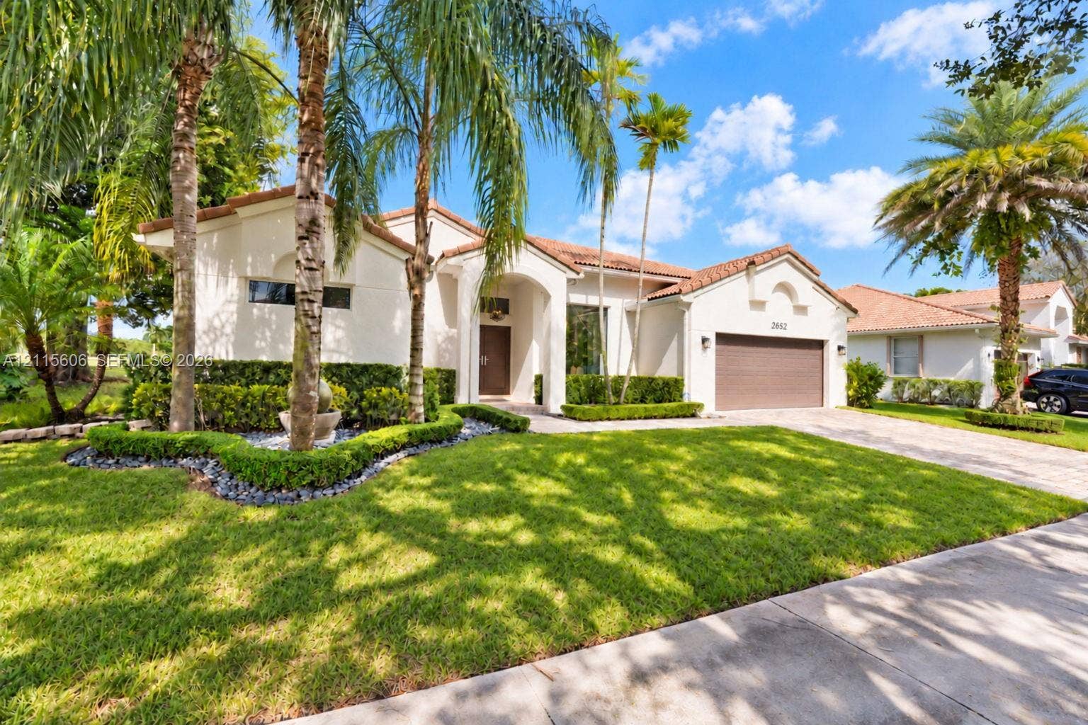 2652 Palmer Place, #2652, Weston, Weston, FL 33332 Stucco exterior featuring a clay tile roof, arched entryway, manicured hedges, and mature palm trees
