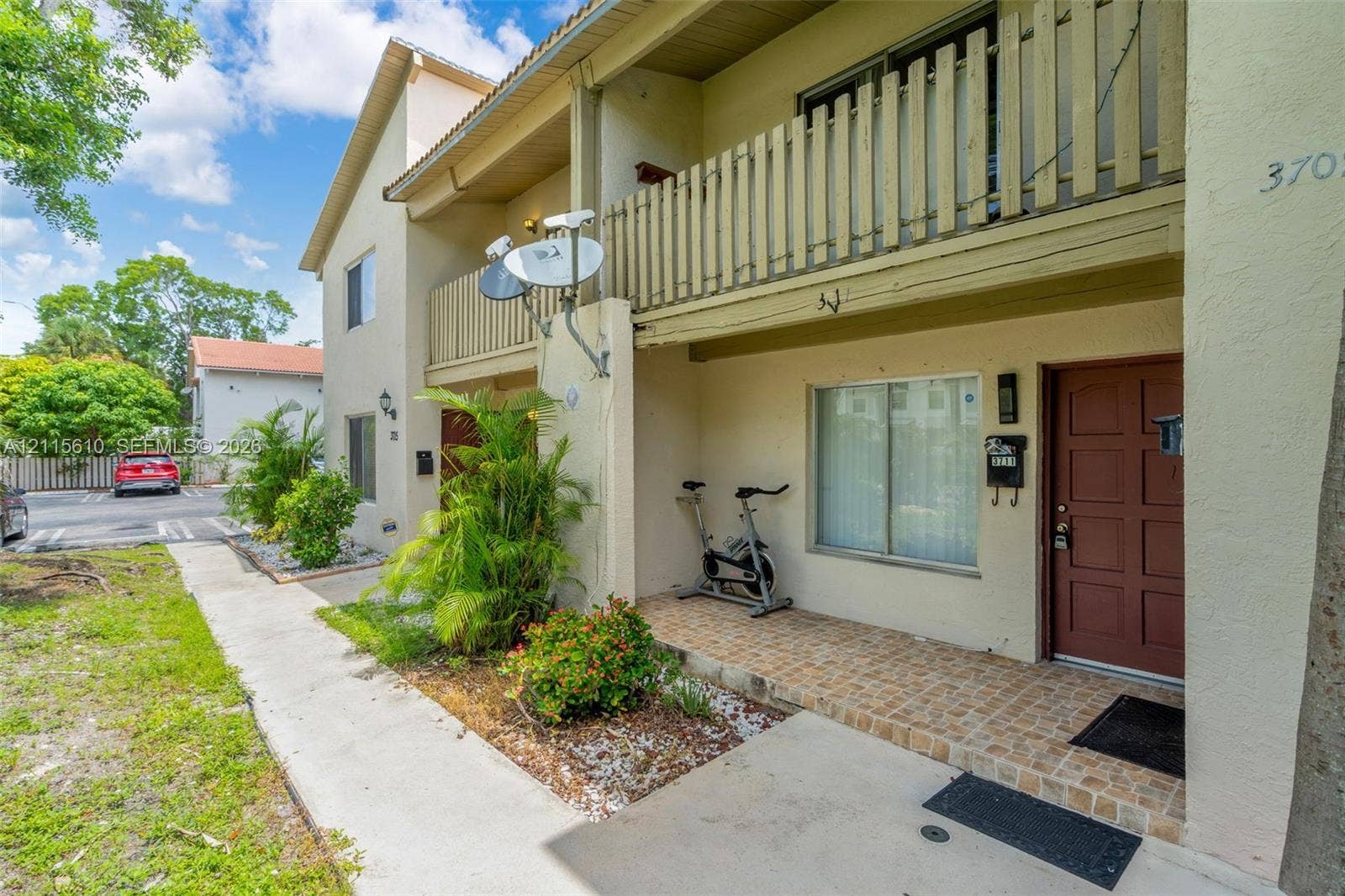 3711 Riverside Drive, Coral Springs, FL 33065 Two-story exterior featuring a stucco facade, covered front porch with tiled flooring, a second-level balcony with vertical slat railing, and a paneled entry door