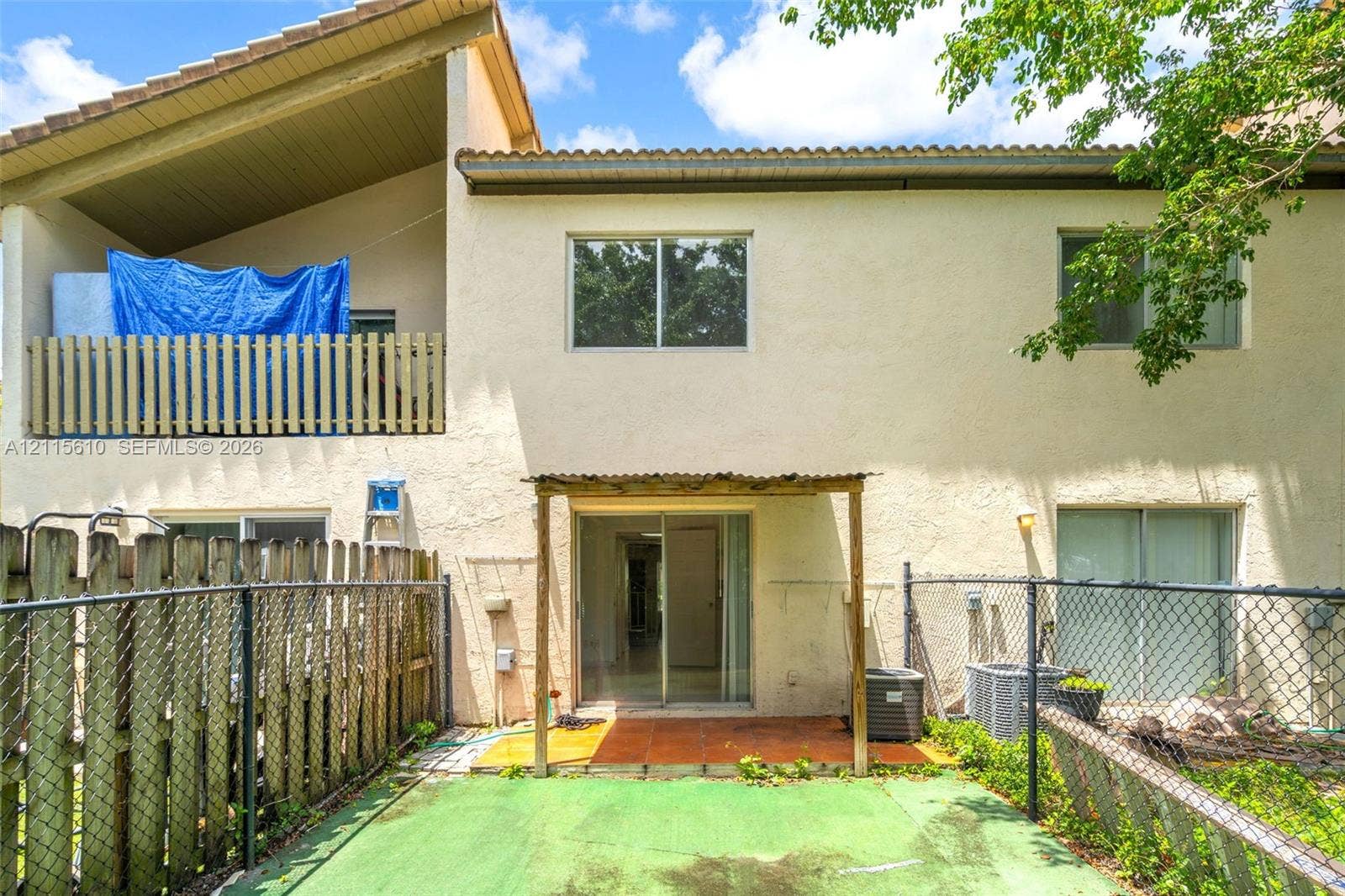 3711 Riverside Drive, Coral Springs, FL 33065 Stucco exterior featuring a covered upper-level balcony with wood-slat railing, a ground-level covered patio with tile flooring, and a fenced yard