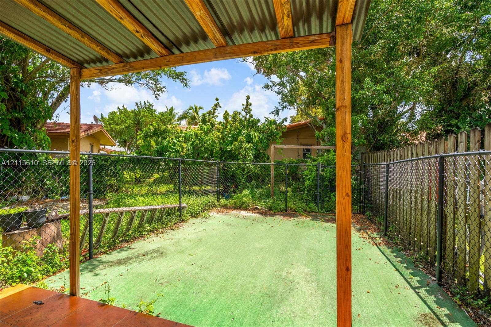 3711 Riverside Drive, Coral Springs, FL 33065 Covered outdoor patio area with a wood-frame structure, metal roofing, green-surfaced concrete flooring, and chain-link fencing
