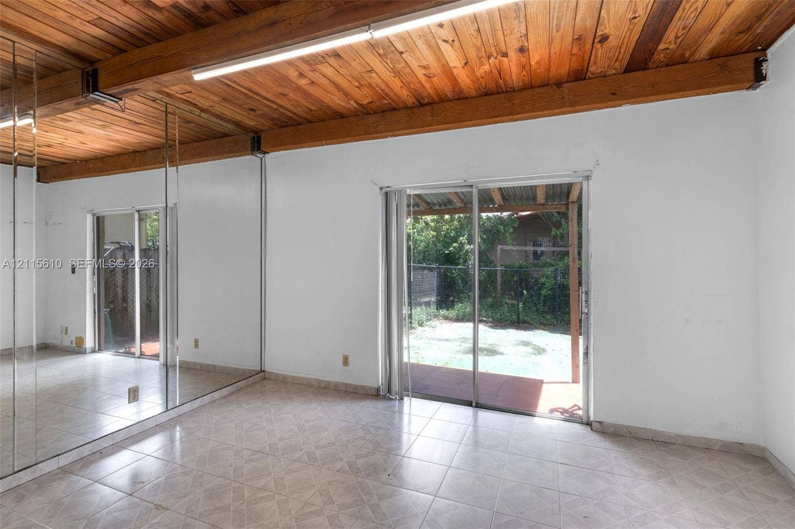 3711 Riverside Drive, Coral Springs, FL 33065 Exposed wood-plank ceiling with structural beams, floor-to-ceiling mirrored walls, ceramic tile flooring, and sliding glass doors leading to a covered patio