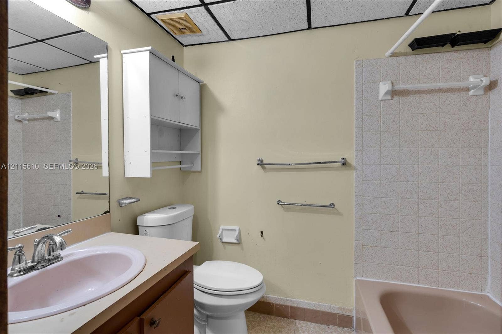 3711 Riverside Drive, Coral Springs, FL 33065 Bathroom featuring an integrated vanity with a basin sink, wall-mounted cabinetry, a bathtub with tiled surround, and chrome hardware throughout