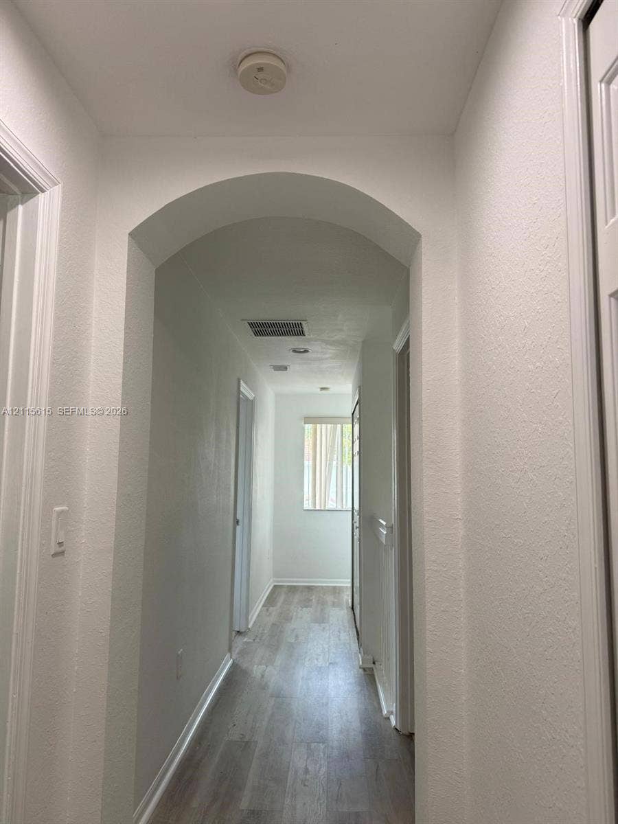 2870 SE 15th Road, #50, Homestead, Homestead, FL 33035 Interior hallway featuring arched architectural detailing, light-toned wood-finish flooring, and crisp white walls