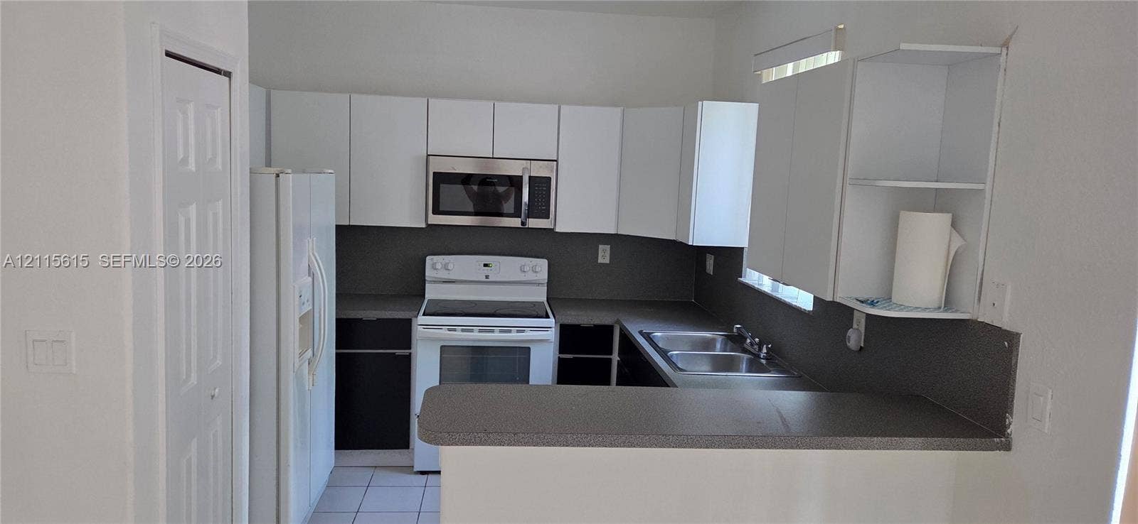 2870 SE 15th Road, #50, Homestead, Homestead, FL 33035 Kitchen featuring white cabinetry, stainless steel microwave, stone-finish countertops, stainless steel dual-basin sink, and a breakfast bar
