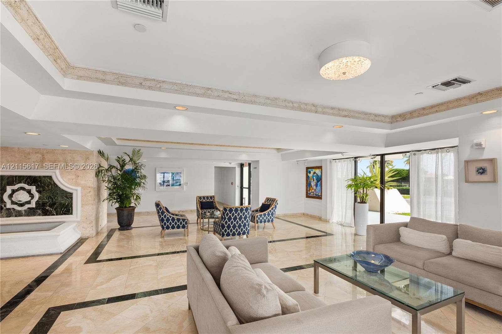Open-concept lobby featuring polished stone flooring with geometric inlays, a recessed tray ceiling with crown molding, a decorative stone-clad wall accent, and a built-in stone fountain