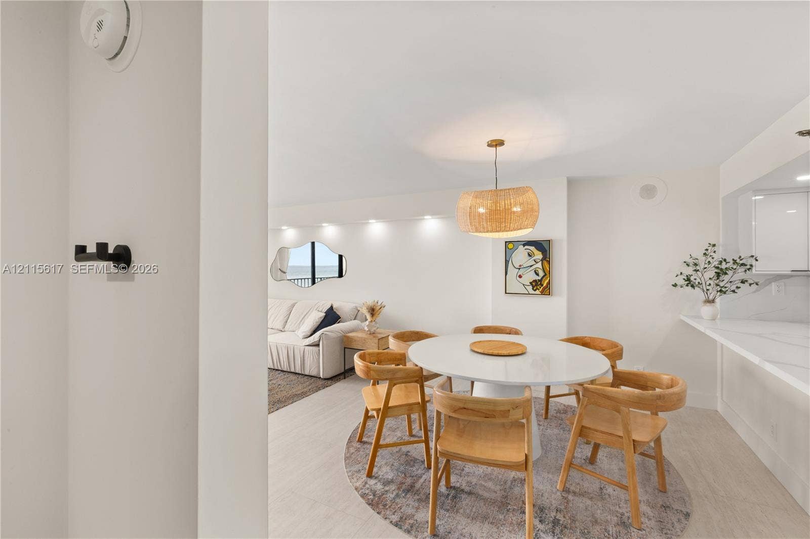 Dining area featuring light-toned flooring, recessed ceiling lighting, a woven drum pendant fixture, and a stone-surface breakfast bar