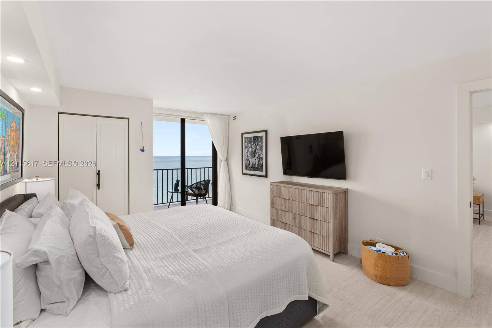 Bedroom featuring light wood-finish flooring, floor-to-ceiling glass door, metal balcony railing, and built-in closet cabinetry