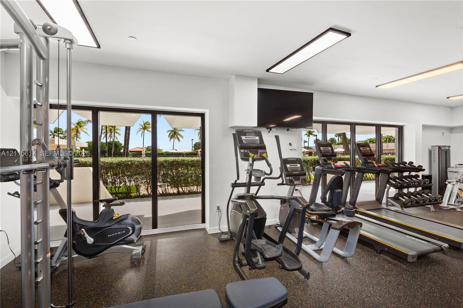 Fitness facility featuring expansive floor-to-ceiling glass sliding doors, recessed linear lighting, speckled composite flooring, and wall-mounted television