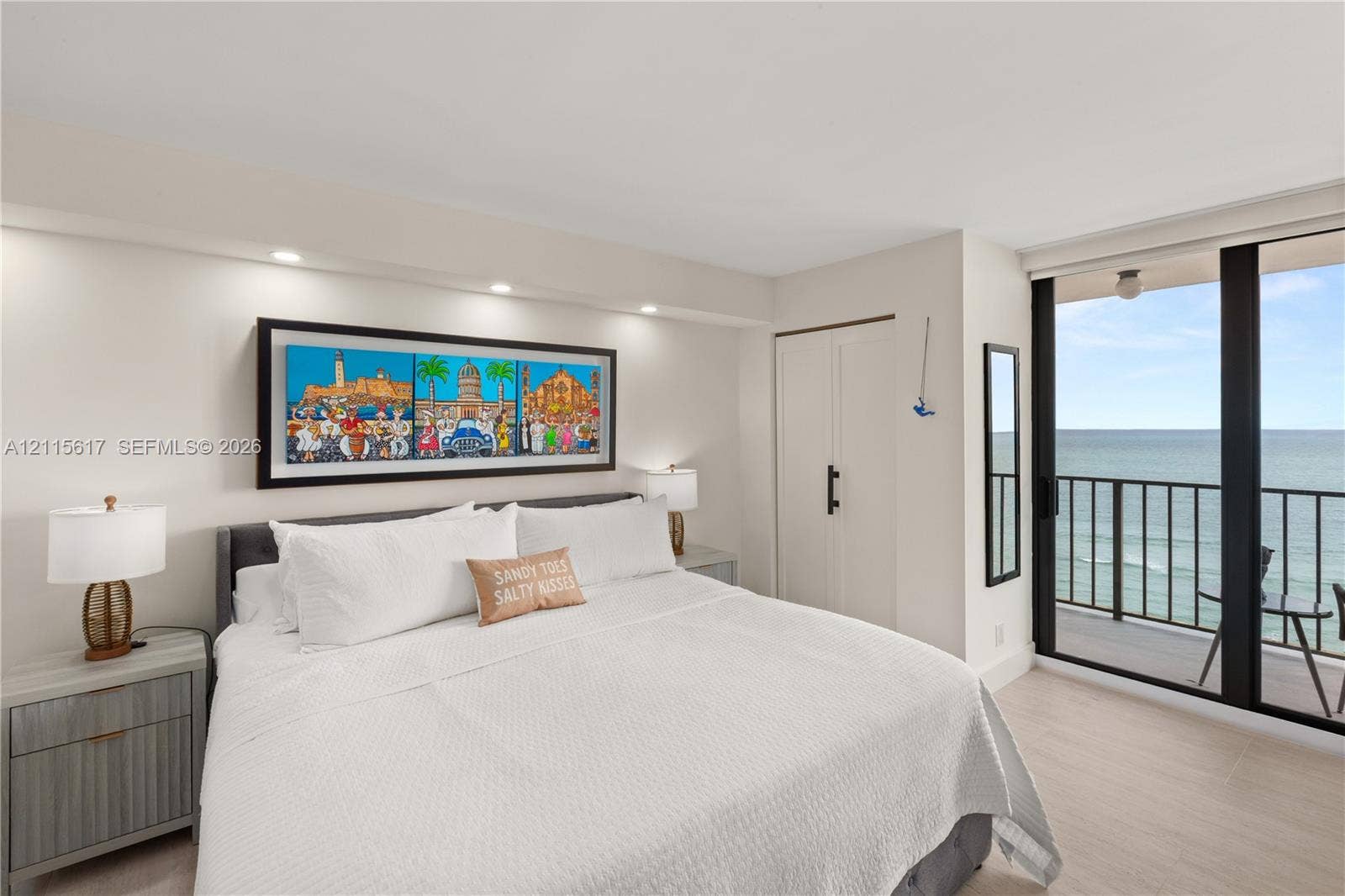 Neutral-toned interior featuring floor-to-ceiling sliding glass doors, a private balcony with metal railing, integrated recessed ceiling lighting, and large-format tile flooring