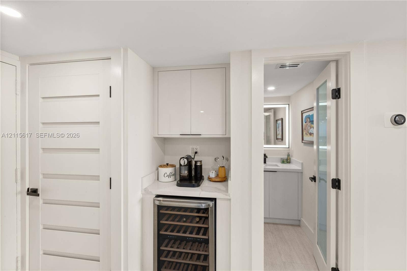 Built-in cabinetry with high-gloss finish, stone countertop, under-counter wine refrigerator, and glass-paneled interior door