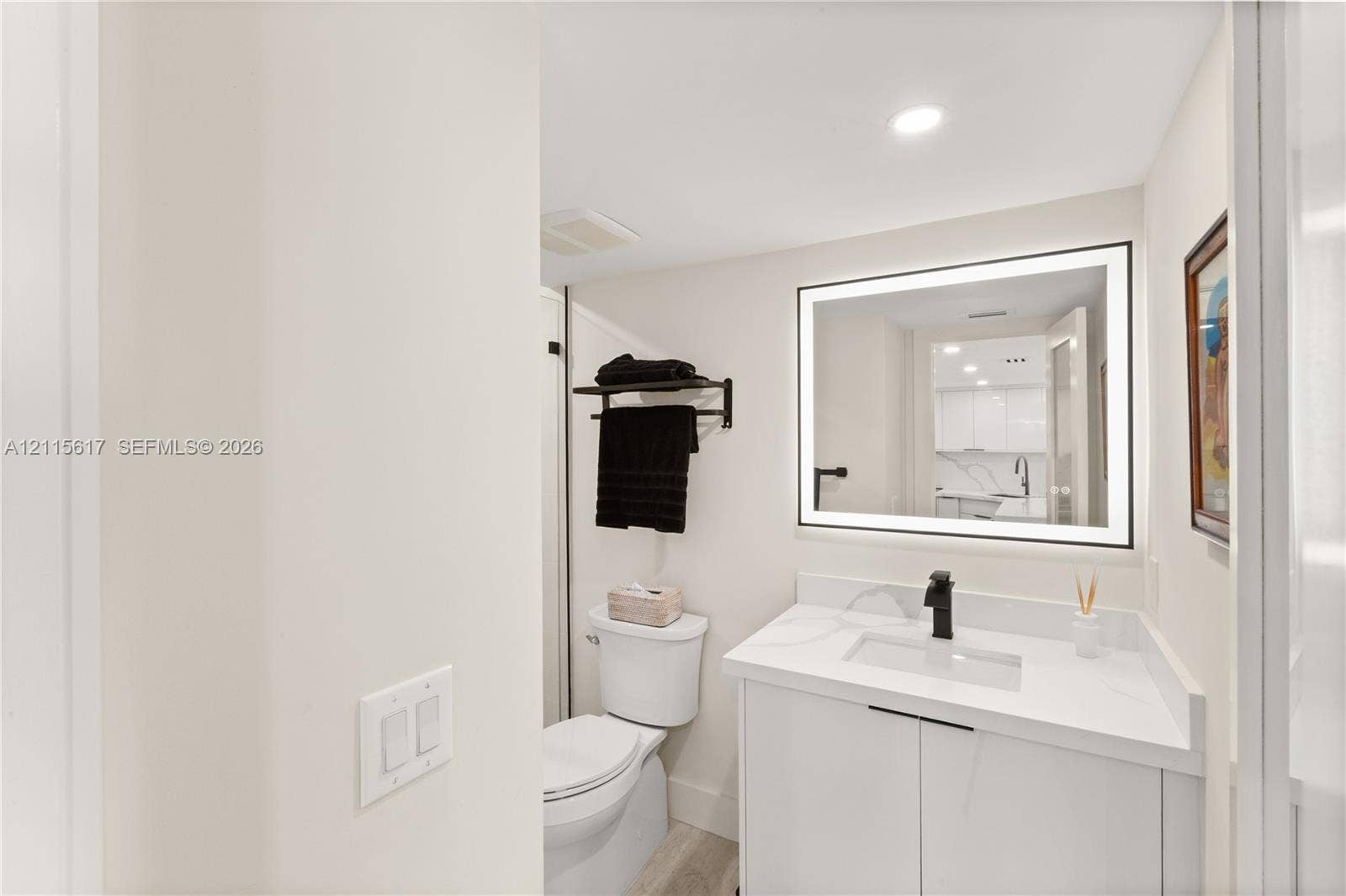 Bathroom featuring a vanity with a white countertop and rectangular integrated sink, matte black faucet, wall-mounted backlit mirror, and two-piece toilet