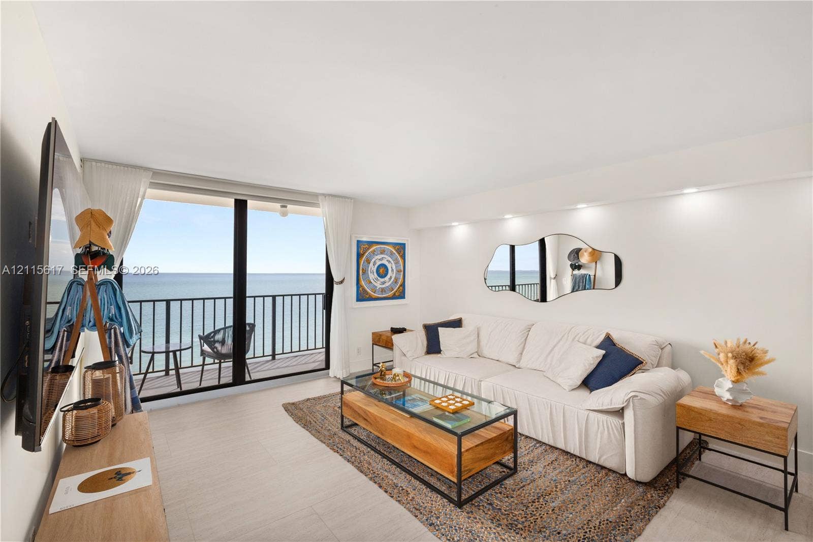Floor-to-ceiling sliding glass doors, private balcony with metal railing, recessed ceiling lighting, wall-mounted accent mirror, and light-tone tile flooring