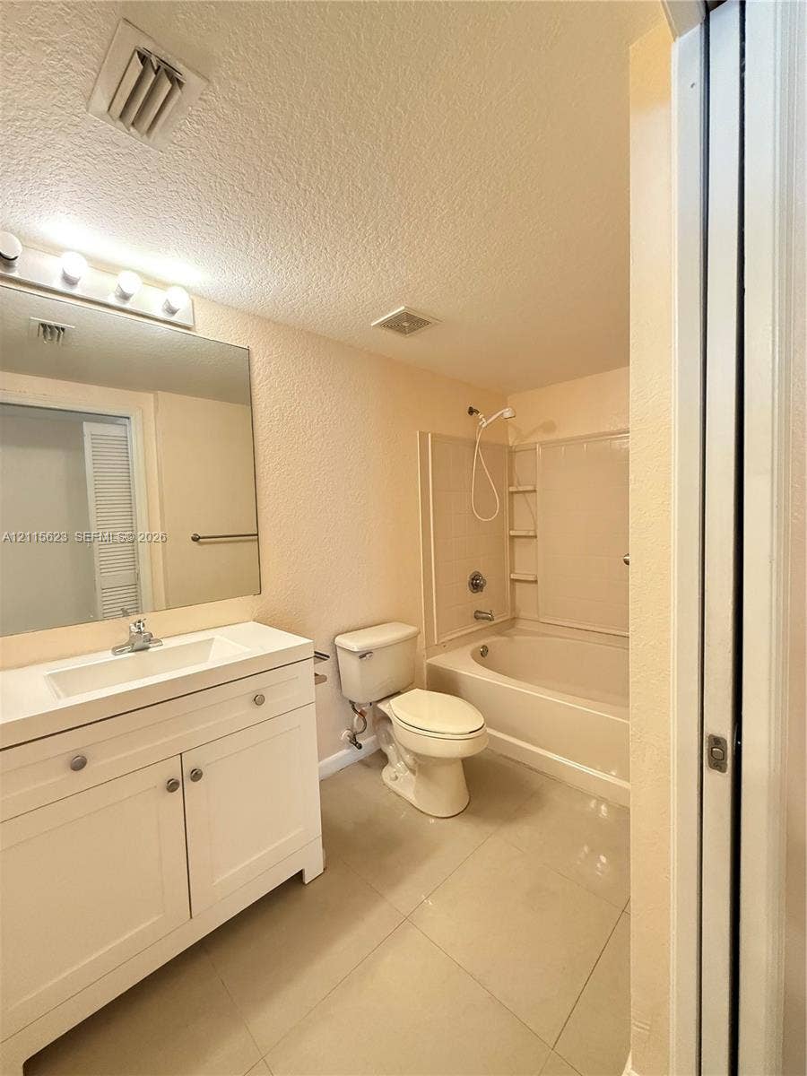 6796 W Sample Road, #6796, Coral Springs, Coral Springs, FL 33067 White vanity featuring a single integrated sink, large-format tile flooring, oversized wall mirror with multi-bulb light fixture, and a built-in tub with integrated shelving