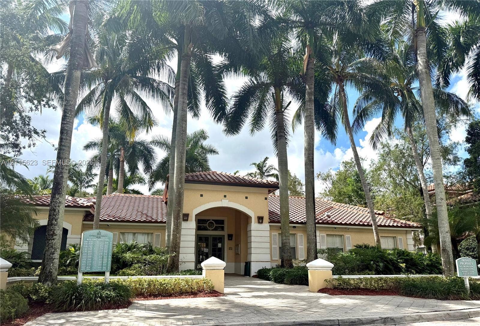 6796 W Sample Road, #6796, Coral Springs, Coral Springs, FL 33067 Stucco exterior featuring a tiled roof, arched entryway, and patterned paver walkway, surrounded by mature palm trees