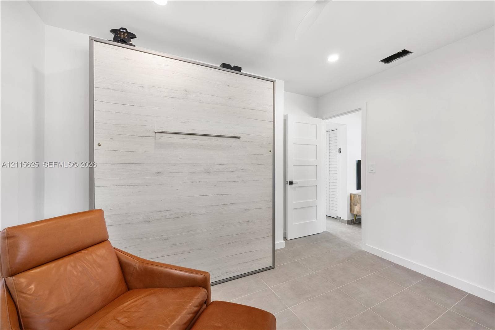 Built-in wall unit with wood-finish paneling, matte black hardware, tile flooring, and five-panel interior door