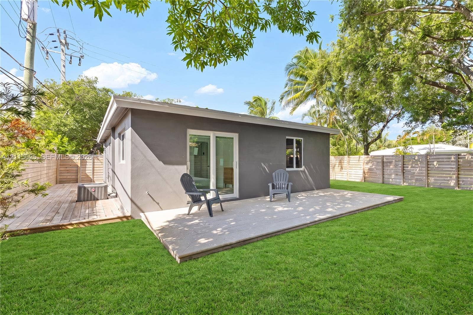 Exterior featuring a stucco facade, expansive wood-finish deck, sliding glass doors, fenced perimeter, and manicured lawn