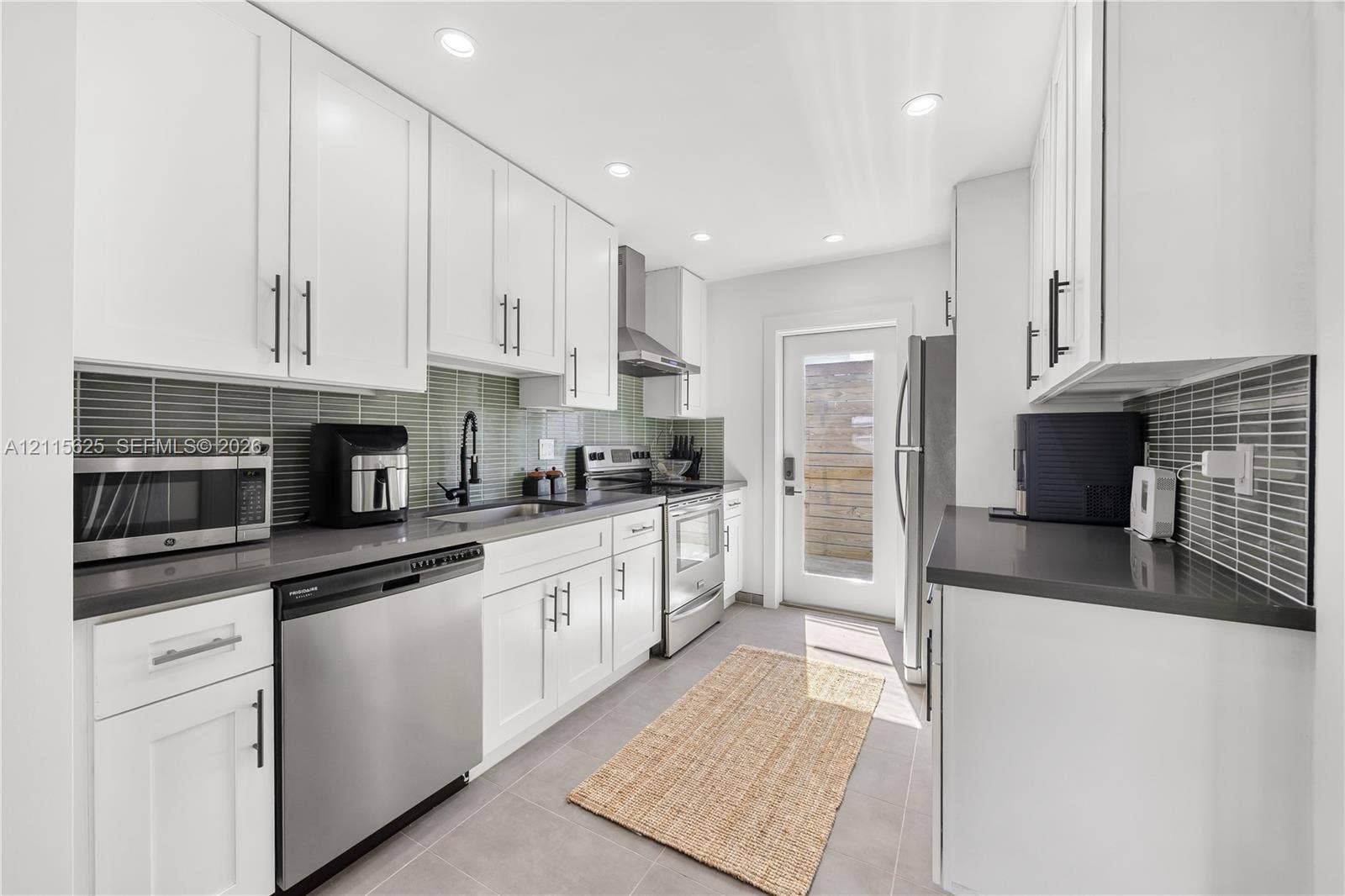 Kitchen featuring white shaker-style cabinetry, matte black hardware, stone-composite countertops, linear glass tile backsplash, and stainless steel appliances