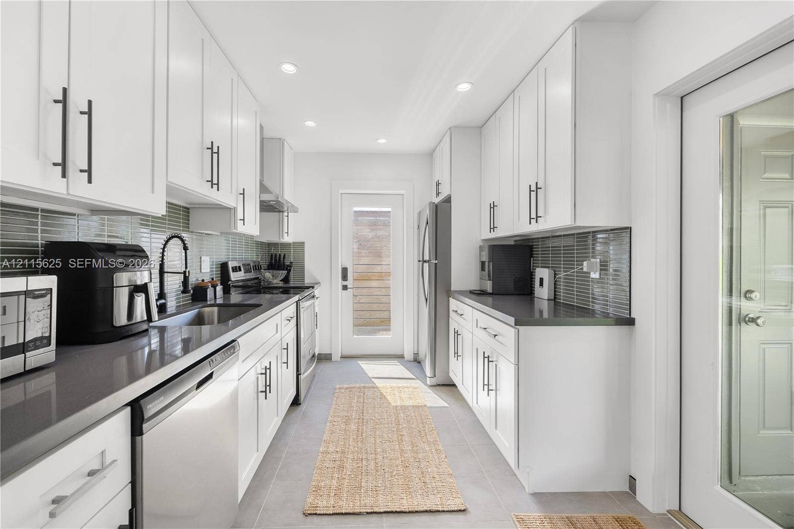 Kitchen featuring white shaker-style cabinetry, dark stone countertops, horizontal glass tile backsplash, stainless steel appliances, and recessed lighting