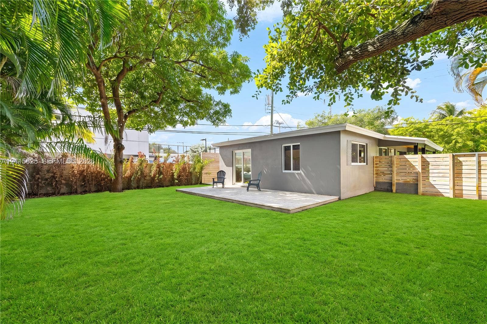 Expansive backyard featuring a level lawn, mature trees, a concrete patio, and perimeter wood fencing