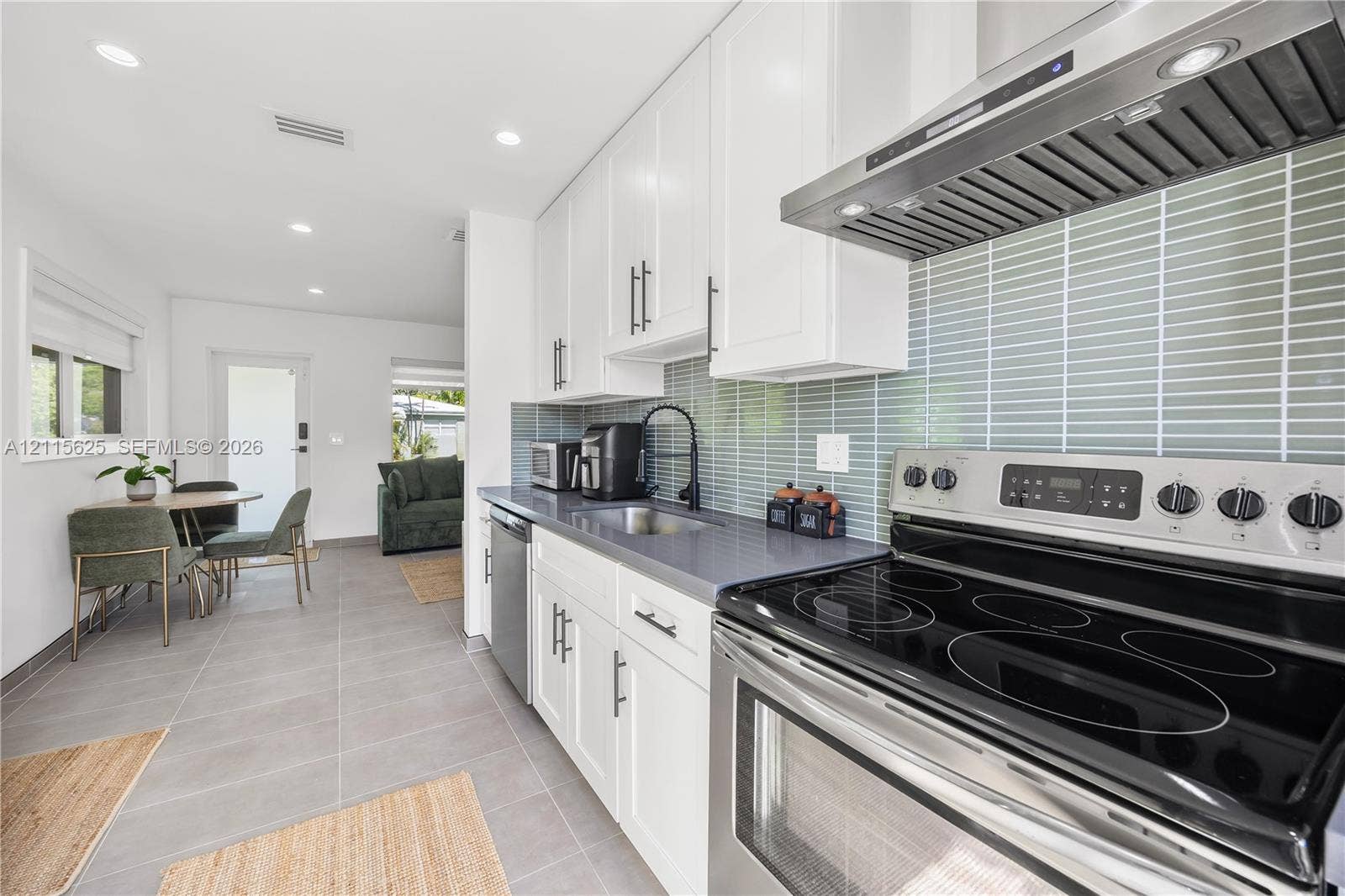 Kitchen featuring white cabinetry, gray solid-surface countertops, a stainless steel range with a built-in exhaust hood, vertical glass tile backsplash, and ceramic tile flooring