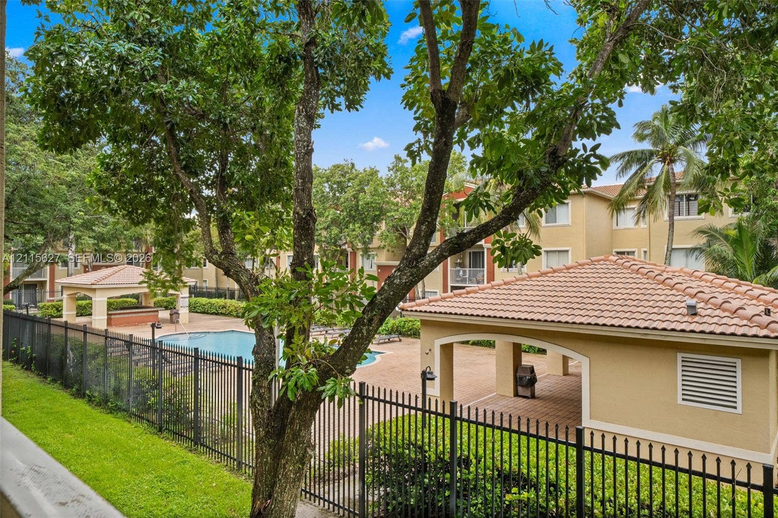 7085 Nova Drive, #218, Davie, FL 33317 Community swimming pool with a covered pavilion featuring a terracotta tile roof, surrounded by mature trees and landscaped grounds enclosed by metal fencing