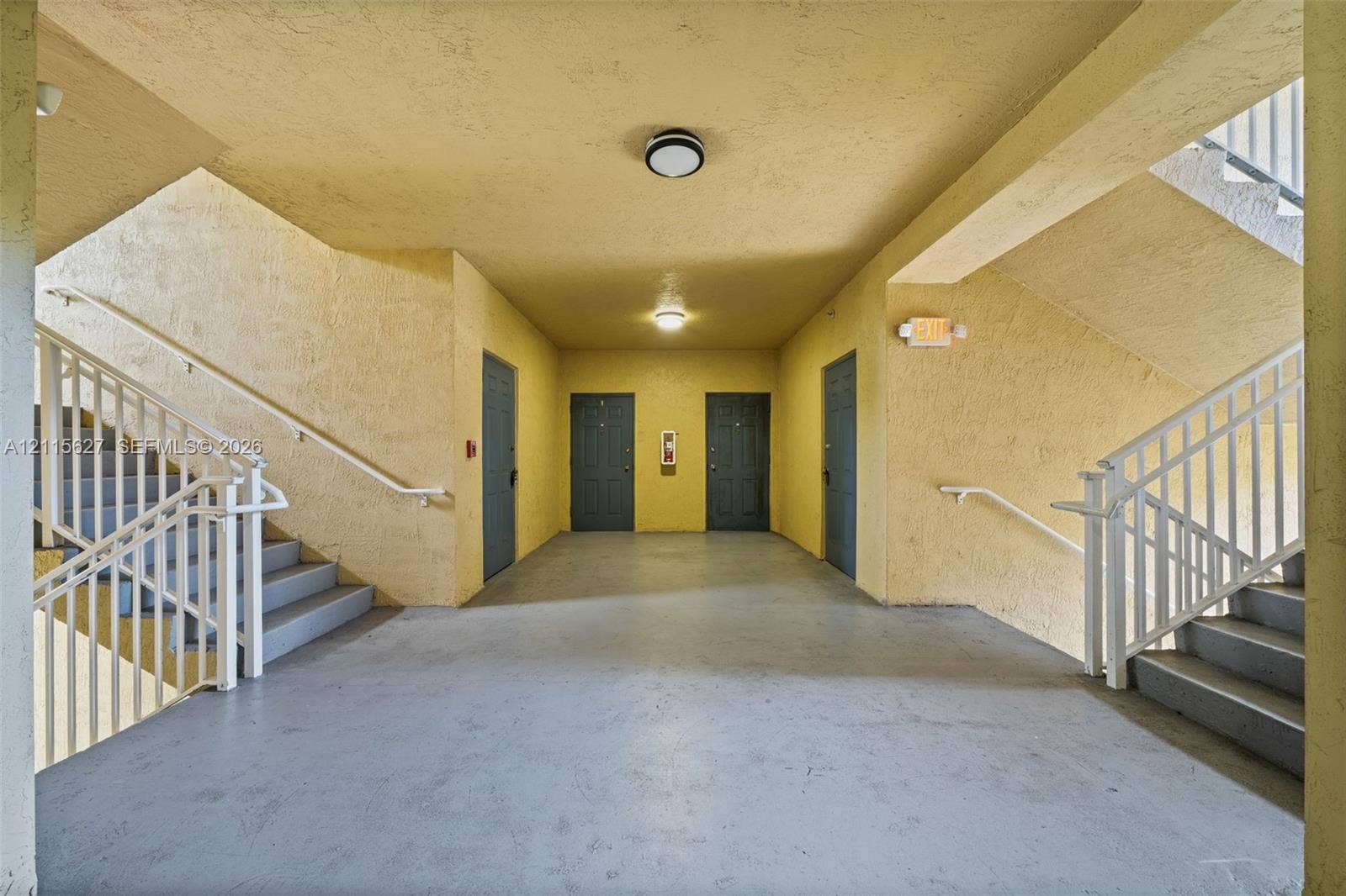 7085 Nova Drive, #218, Davie, FL 33317 Covered common area featuring textured walls, solid surface flooring, dual staircases with metal railings, and flush-mount ceiling lighting