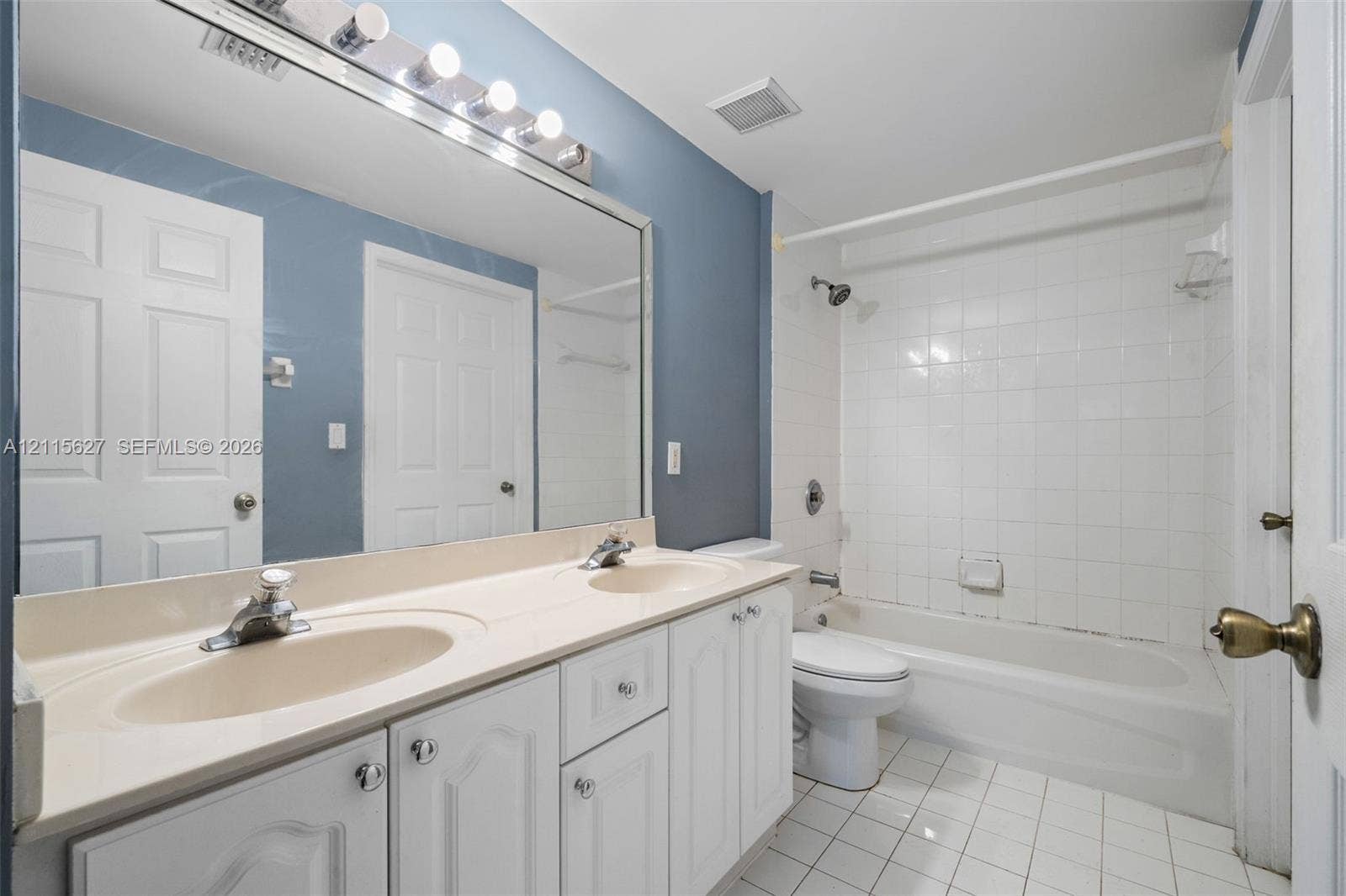 7085 Nova Drive, #218, Davie, FL 33317 Bathroom featuring a dual-sink vanity with a solid-surface countertop, full-width vanity mirror, tile-surround bathtub, and ceramic tile flooring