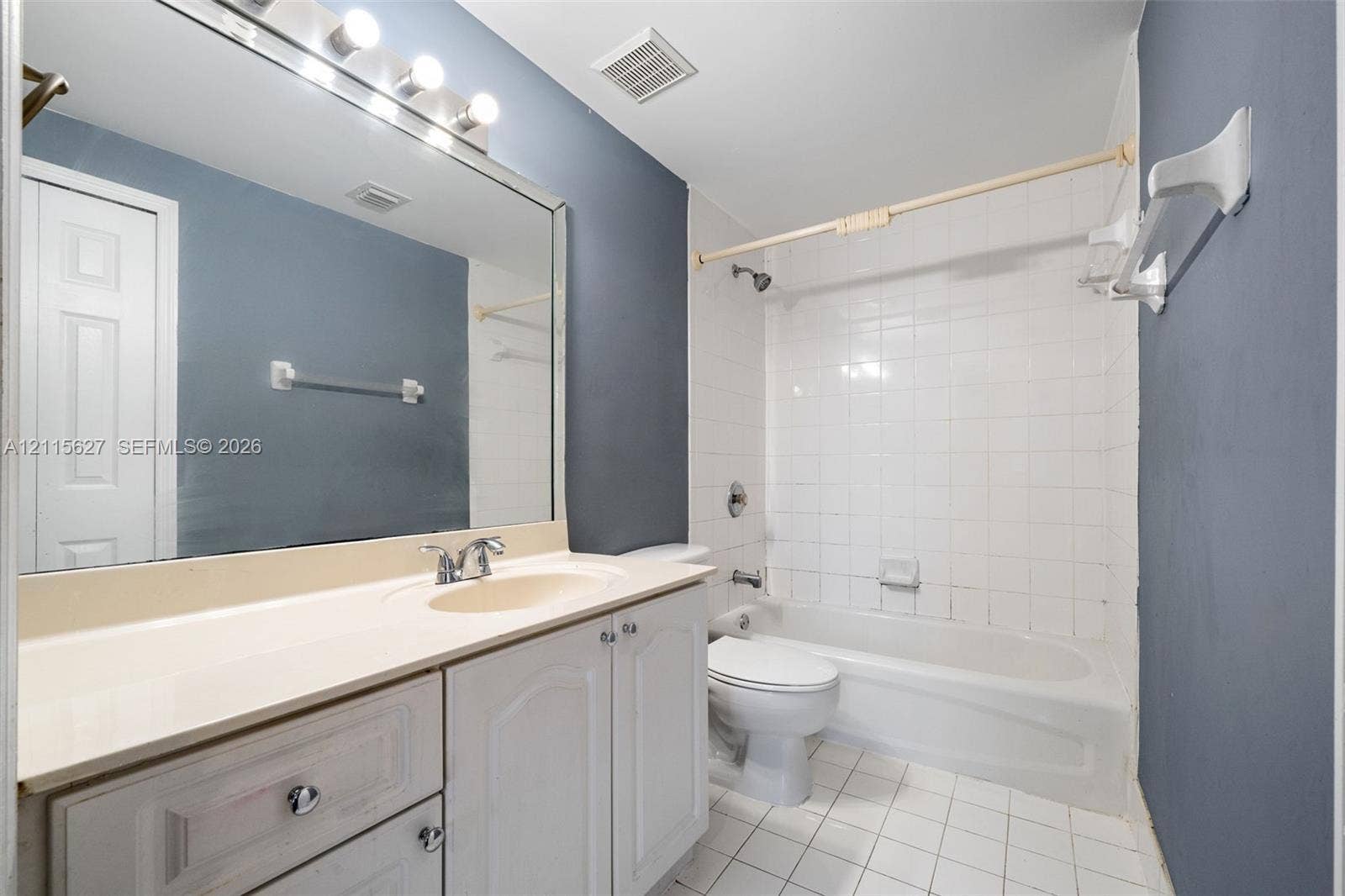 7085 Nova Drive, #218, Davie, FL 33317 Bathroom featuring white cabinetry, integrated sink, vanity-width wall mirror, chrome-finish plumbing fixtures, and a tiled tub surround