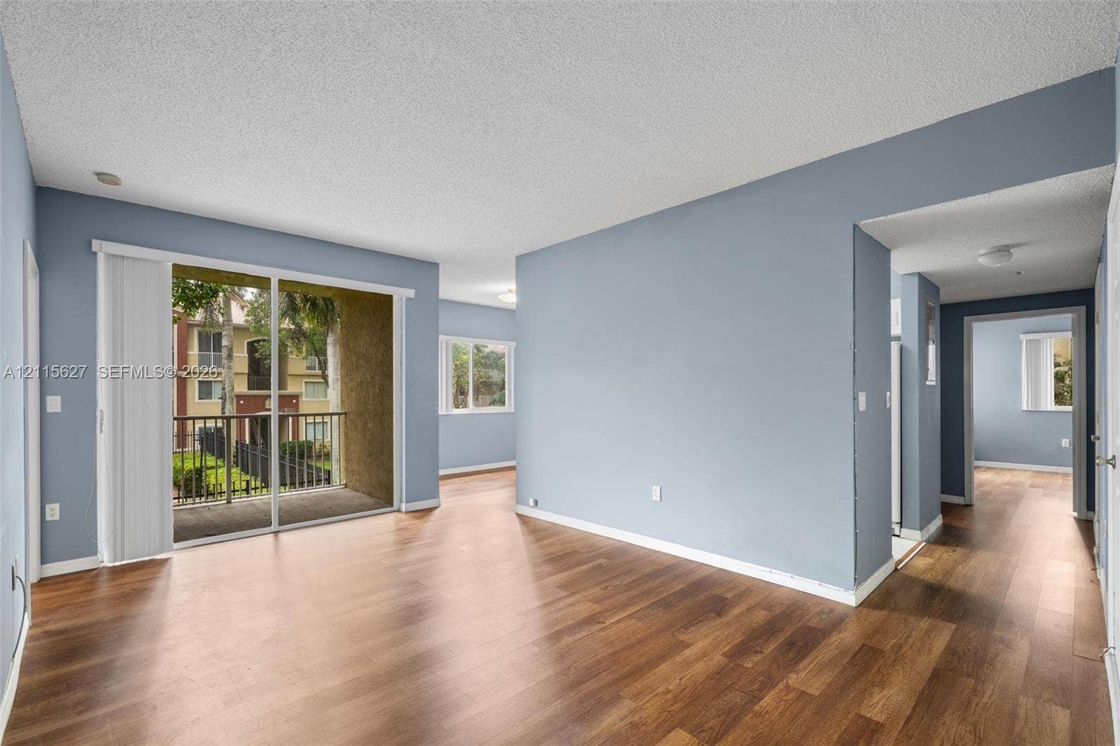 7085 Nova Drive, #218, Davie, FL 33317 Open-concept interior featuring wood-finish flooring, sliding glass door access to a private balcony, and neutral paint palette