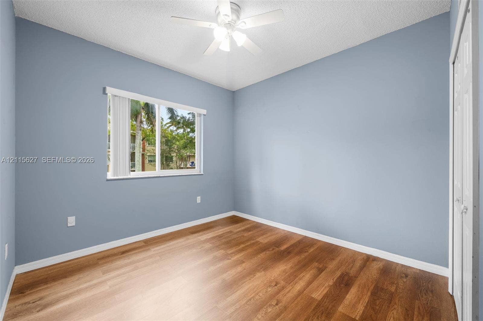 7085 Nova Drive, #218, Davie, FL 33317 Room featuring wood-finish flooring, light blue wall paint, a ceiling fan with integrated lighting, and a white sliding-door closet