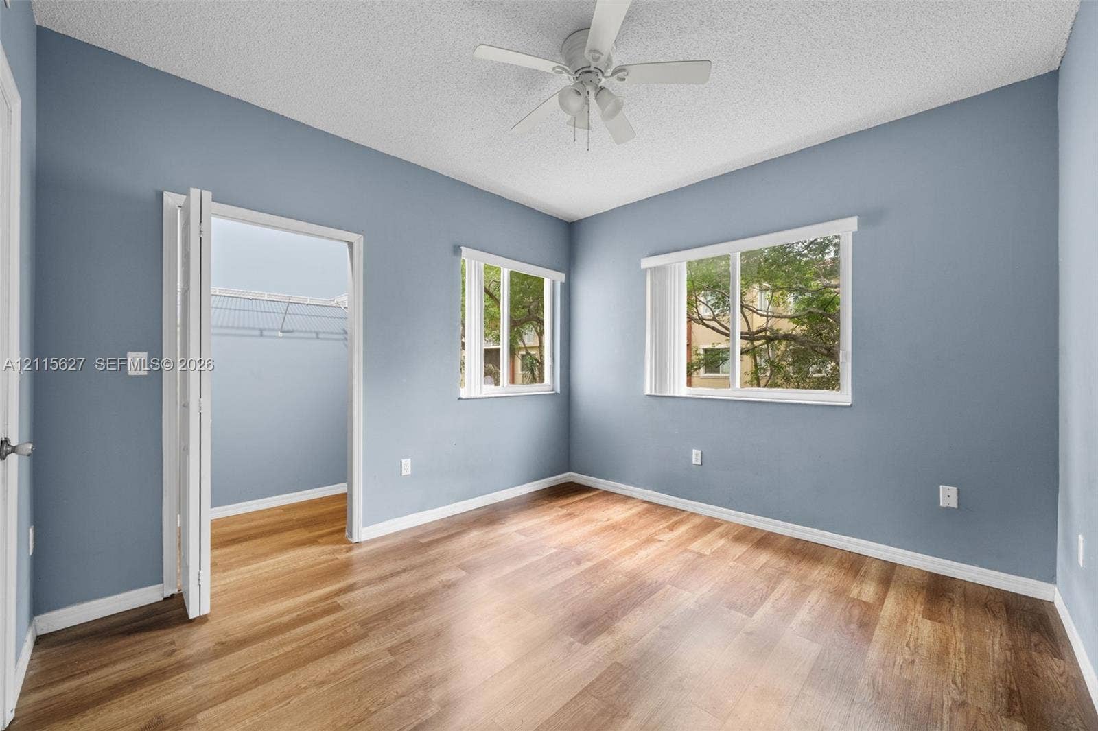 7085 Nova Drive, #218, Davie, FL 33317 Room featuring wood-finish flooring, two windows, a ceiling fan with integrated lighting, and a closet with bifold doors