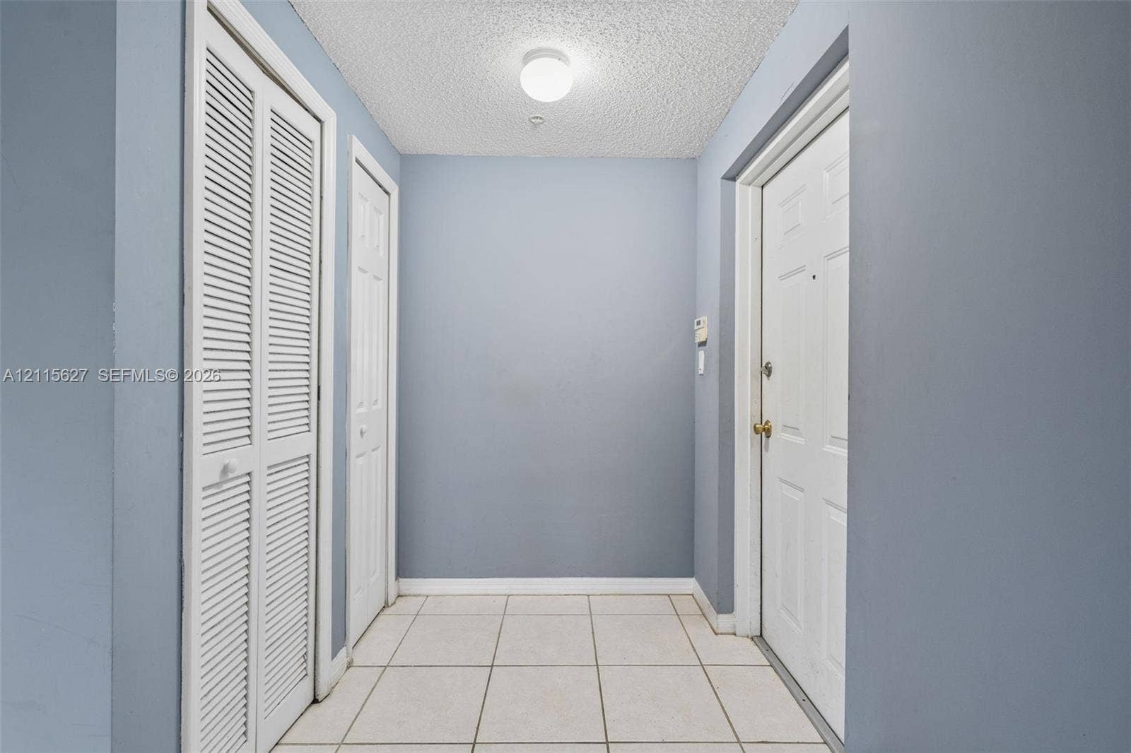 7085 Nova Drive, #218, Davie, FL 33317 Entryway featuring white tile flooring, louvered bi-fold closet doors, a paneled interior door with metal hardware, and a ceiling-mounted light fixture