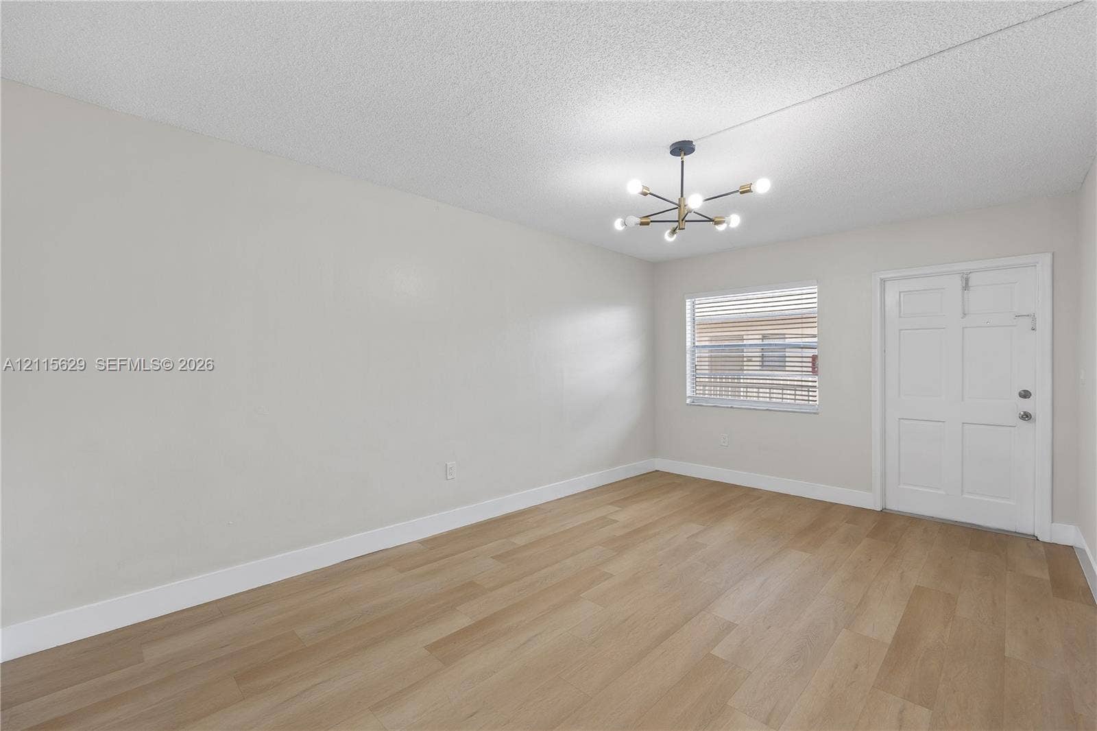Neutral-toned interior featuring wood-finish flooring, a multi-arm modern pendant light fixture, and a white six-panel door